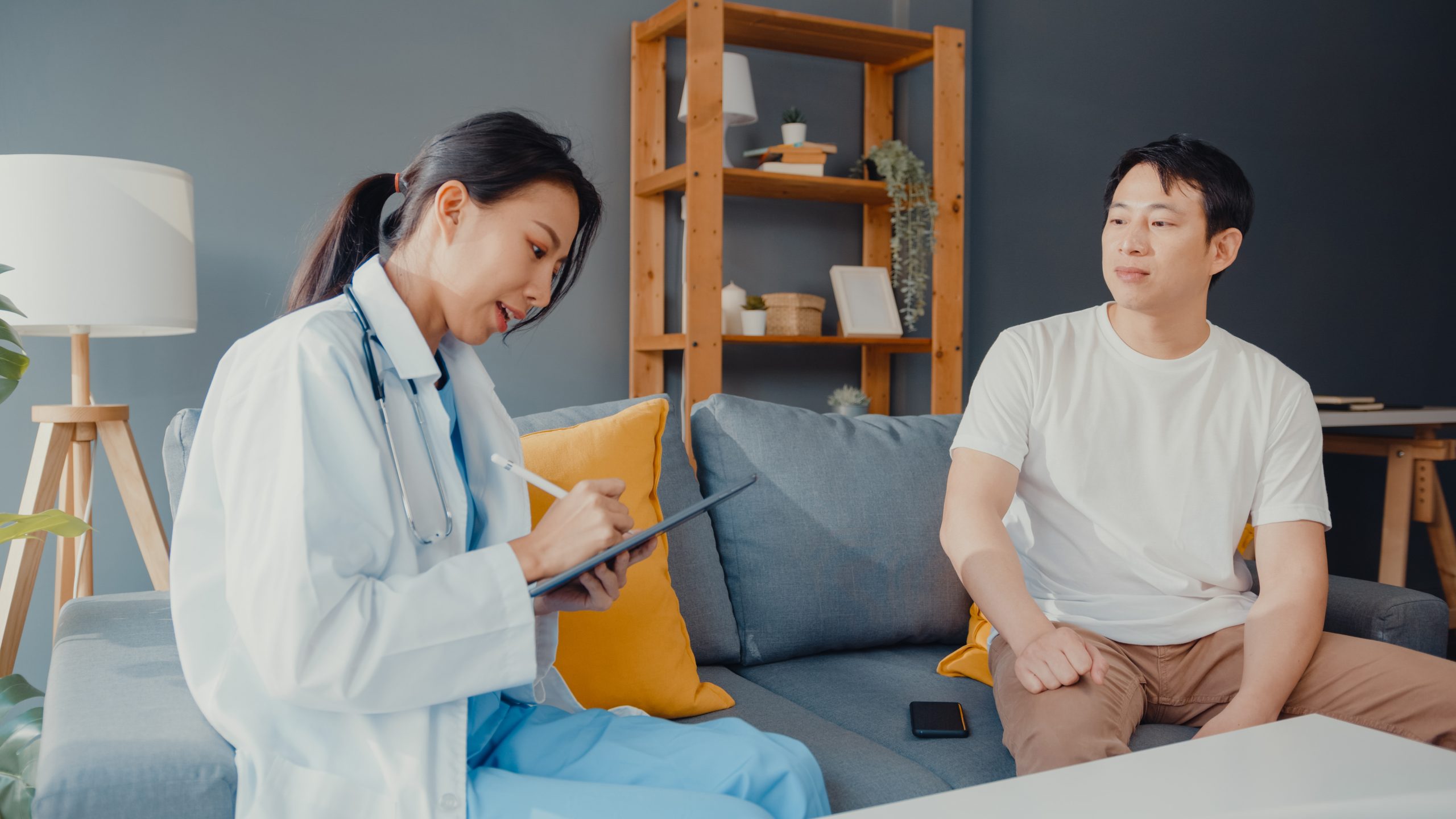 young-asia-female-professional-physician-doctor-using-digital-tablet-sharing-good-health-test-news-with-happy-male-patient-sit-couch-house-scaled.jpg