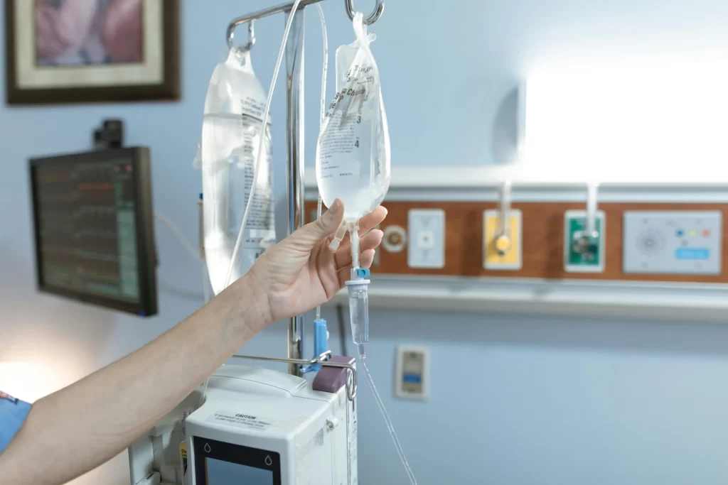 A person's hand adjusting a clear IV fluid bag hanging on a stand in a hospital setting.